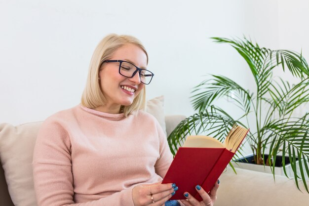 Happy albino woman relaxing at home in cozy winter or autumn weekend with book and cup of hot tea, sitting in sofa