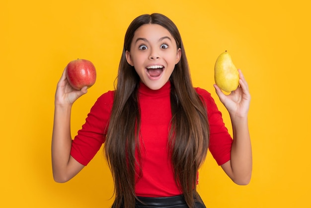 Happy amazed child hold fresh apple and pear on yellow background