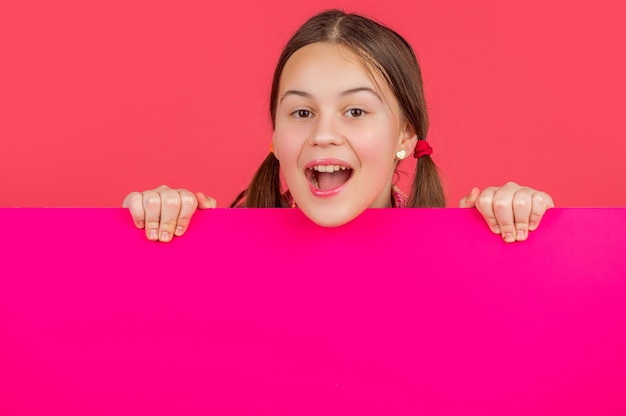 happy amazed kid behind blank pink paper with copy space for advertisement