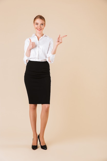 Happy amazing young business woman pointing showing thumbs up.