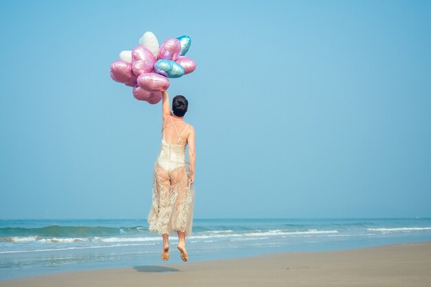 사진 행복하고 젊은 여성은 더 밝고 찬란한 공기 풍선을 들고 짧은 머리와 함께 존재합니다. 해변에서 쉬고 있는 소녀의 손에 있는 밝은 공.