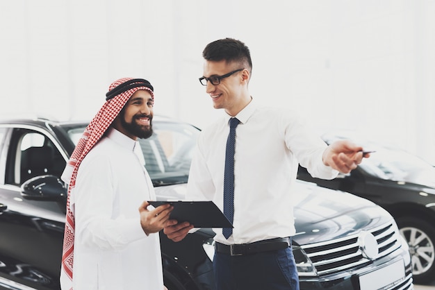 Happy Arab in Car Showroom Agent Holds Papers.
