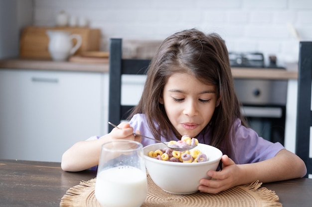 Happy arab child girl having breakfast colorful cereal with milk at home on the morning