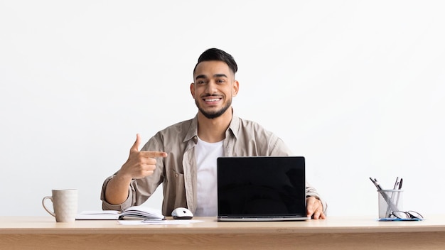 Happy arab guy showing laptop with black empty screen mockup