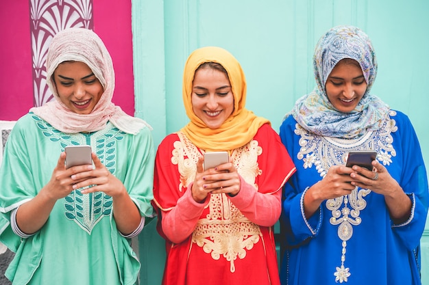 Счастливые арабские друзья, использующие смартфоны на открытом воздухе - молодые исламские девушки веселятся с новой технологией тренда - концепция влияния и дружбы - сосредоточьтесь на лицах