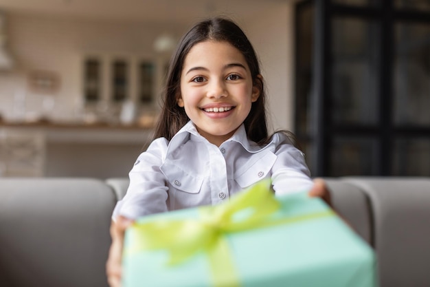 Happy arabic girl giving present to camera sitting at home