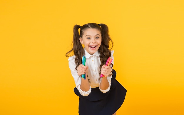 Happy arts Happy little artist Happy girl holding colorful markers on yellow background Cheerful small child with happy smile and drawing pens Enjoying arts and crafts