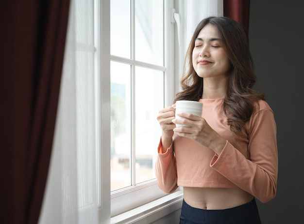 Foto donna felice dell'asia che tiene il caffè in tazza nel soggiorno di casa