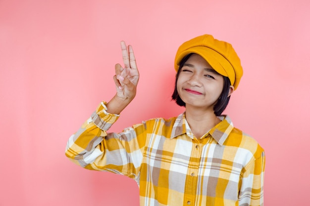 Happy asia young girl wear yellow shirt and yellow hat point up with pink background.