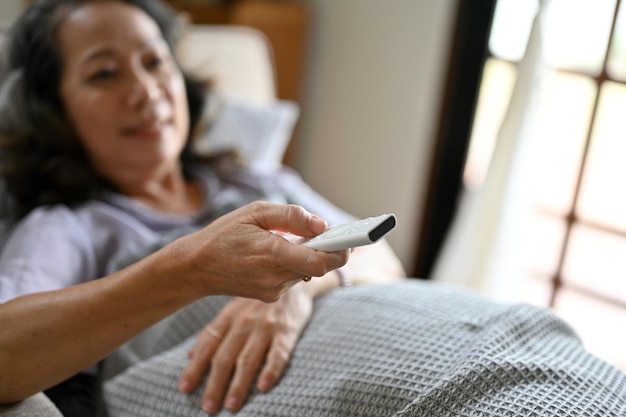 TV 리모컨을 들고 소파에 누워 있는 행복한 아시아 60대 여성