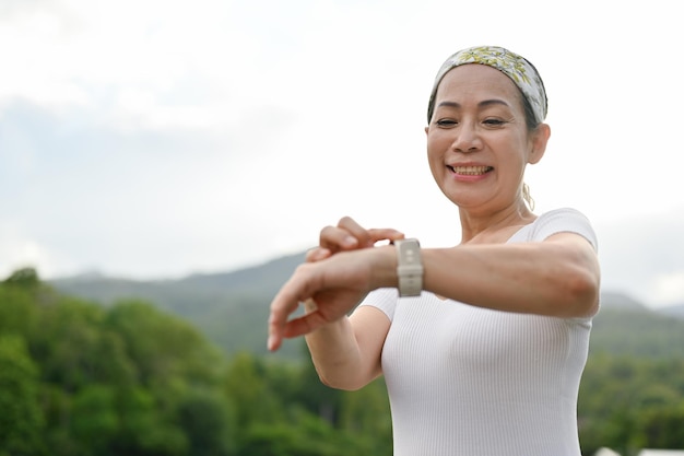 Happy Asian aged woman enjoy exercising outside checking her heart rate on a smartwatch