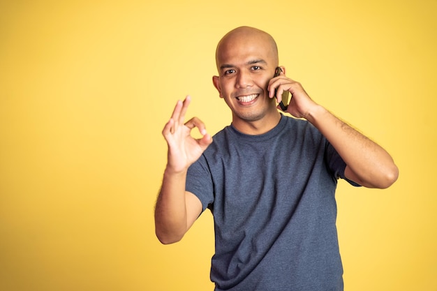 Uomo calvo asiatico felice che mostra il gesto giusto che fa telefonata