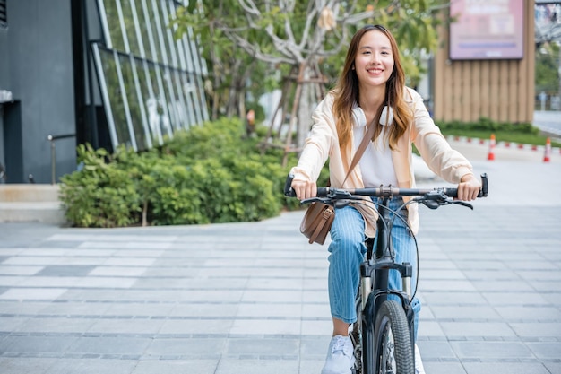 建物の街の近くの屋外の通りで自転車に乗って幸せなアジアの美しい若い女性