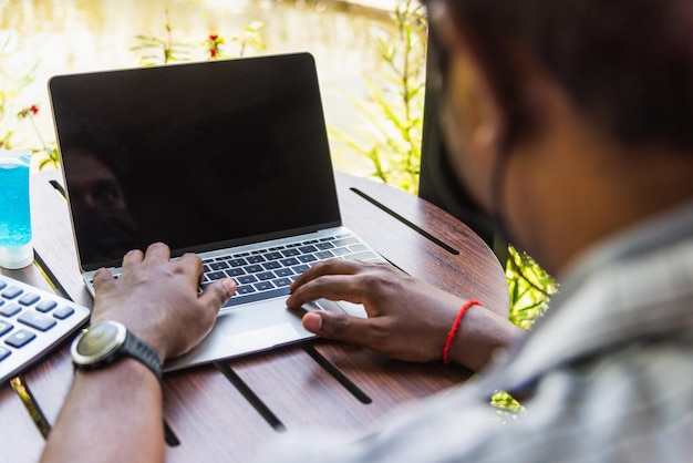 Happy Asian black businessman person or office worker wear face mask protect sitting on desk work from home using laptop computer typing keyboard and connect networking online at the coffee cafe shop