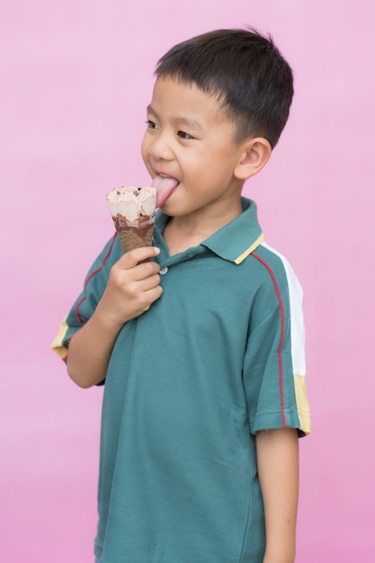 Happy asian boy holding ice cream chocolate cone and licking on pink background