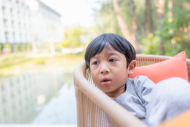 幸せなアジアの少年は、椅子に座って指を上に向けて楽しんで笑っています幸せな家族や養子縁組や子育ての成功の概念