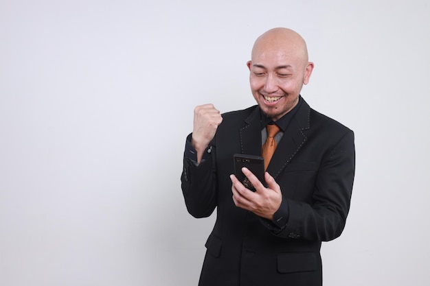 幸せなアジア人ビジネスマンが携帯電話を見ていると興奮して拳を握っている.