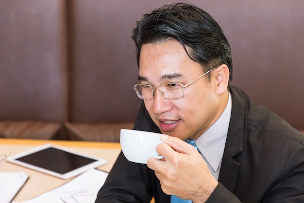 Uomo d'affari asiatico felice che beve caffè in ufficio