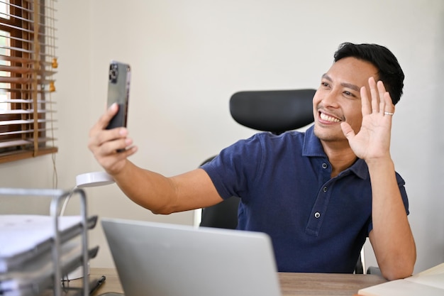 Happy Asian businessman having a video call with his girlfriend while sitting in the office