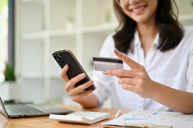 Happy Asian businesswoman at her office desk holding a mobile phone and a credit card