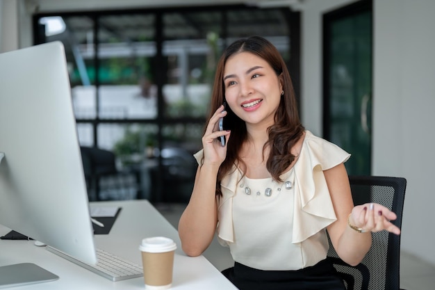 A happy Asian businesswoman is enjoying talking on the phone while sitting at her desk