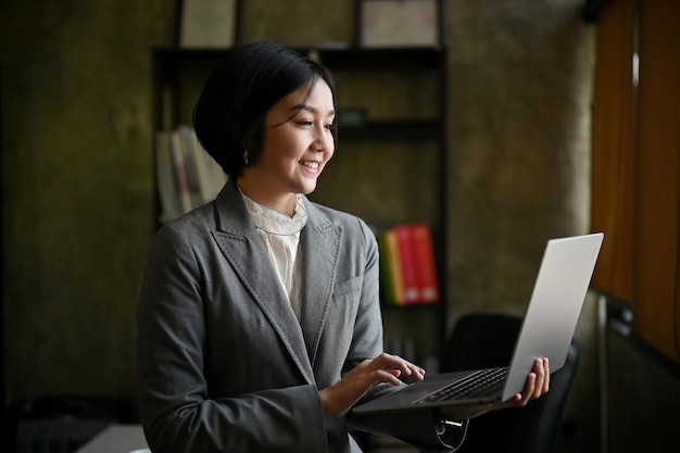 A happy Asian businesswoman leaning on her table and using her portable laptop computer