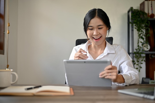 A happy Asian businesswoman working on her work on al tablet at her desk