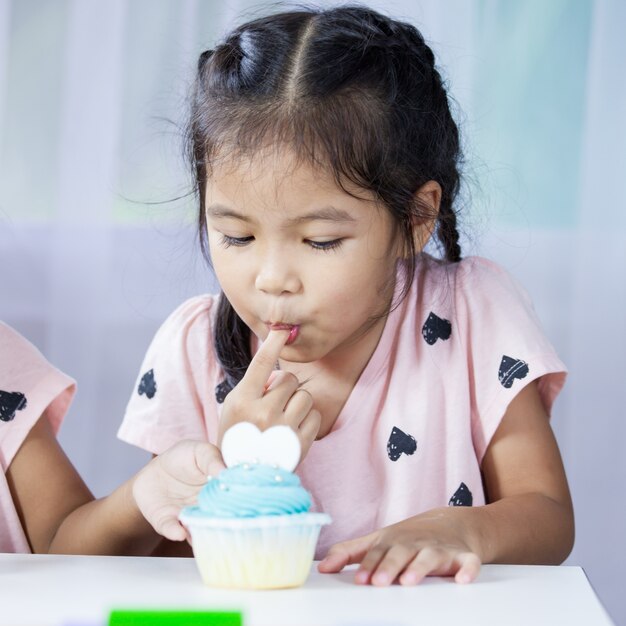 おいしい青いカップケーキを食べる幸せなアジアの子供の女の子