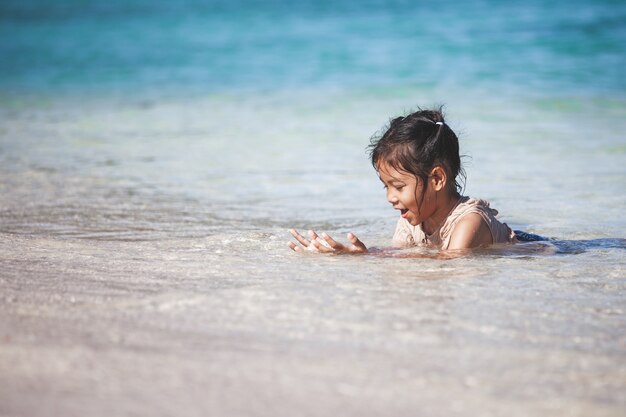 Happy asian child girl having fun to play water in the beautiful sea in summer vacation