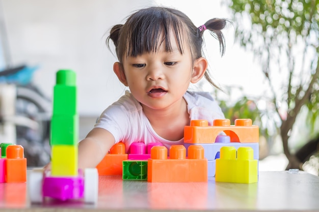 Фото Счастливая азиатская девочка ребенка играя пластмассовые игрушки блока. концепция обучения и образования. улыбающийся малыш.