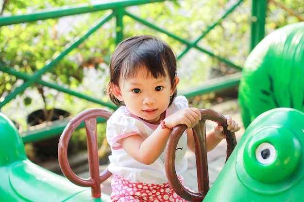 Ragazza asiatica felice del bambino che gioca i giocattoli al campo da giuoco. lei sorride.