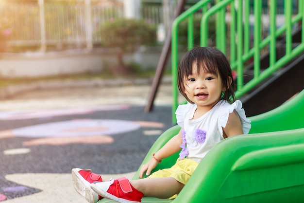 웃 고 웃 고 행복 한 아시아 아이 소녀. 그녀는 놀이터에서 슬라이더 바 장난감을 가지고 노는.