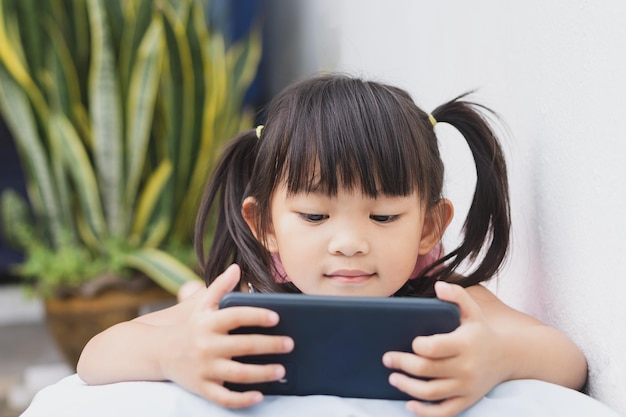 Foto ragazza asiatica felice del bambino che guarda e utilizza lo smartphone