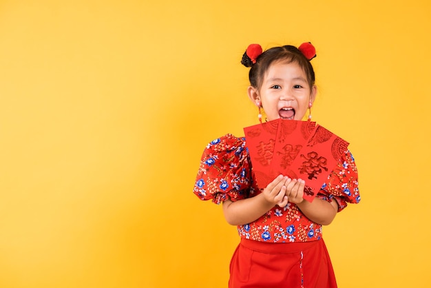 幸せなアジアの中国の小さな女の子の笑顔は赤いチョンサムチャイナドレスを着てangpao赤いパケットの金銭的な贈り物を保持します