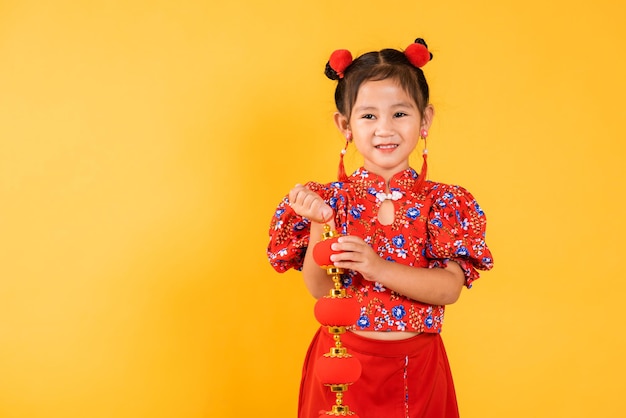シルクのランタンを保持している赤いチャイナドレスを身に着けている幸せなアジアの中国の少女の笑顔