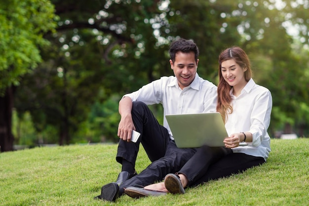 Photo happy asian couple college working via technology laptop with laughing action in the park