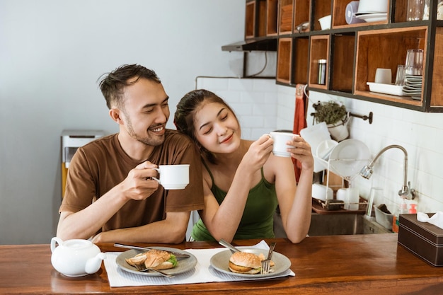 Happy asian couple drinking coffee in cups together in kitchen