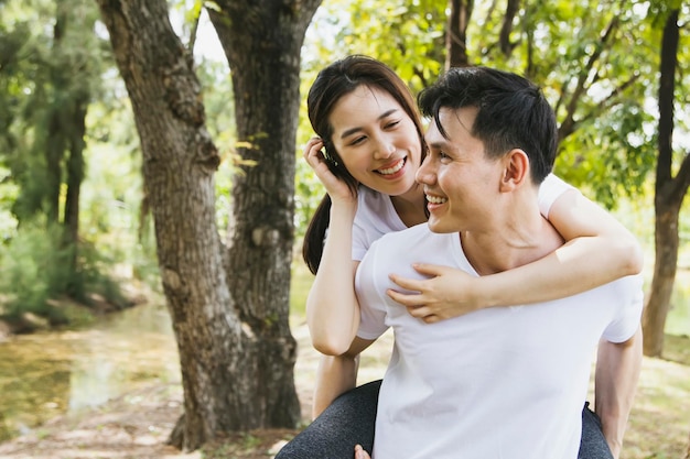 Happy Asian couple having fun playing and riding their necks while strolling in the park