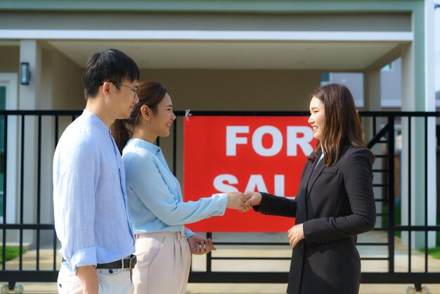 Happy Asian couple looking for their new house and shake hands with real estate broker after a deal. Young couple handshaking real estate agent after signing contract for buy house.