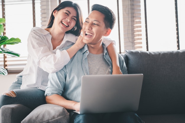 happy Asian couple in love laughing while using laptop