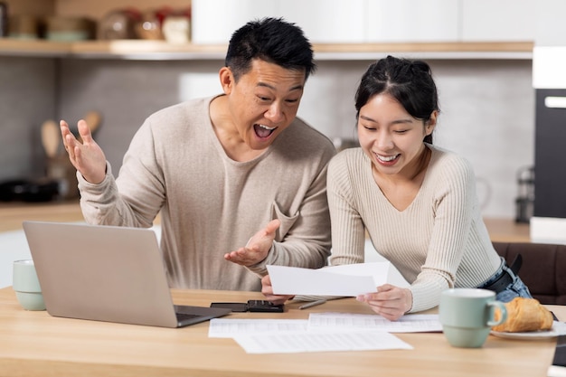 Happy asian couple paying bills online using computer