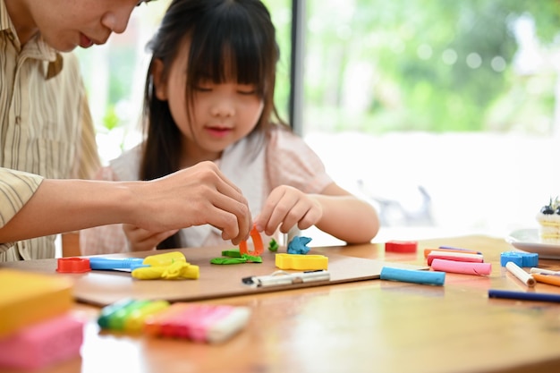 Happy Asian dad and daughter enjoys moulding colorful clay or play dough together at home