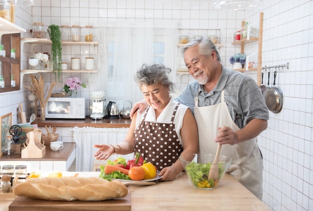 Happy asian elder senior couple cooking fresh meal in kitchen at home.