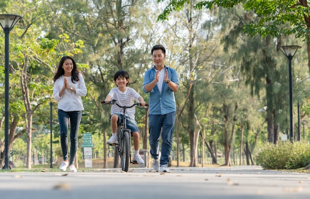 幸せなアジアの家族の父と母が公園で自転車に乗ることを息子に教えています