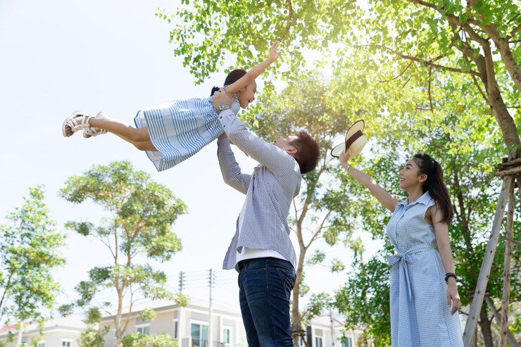 Photo アジアの幸せな家族。父は自然の日差しと家の公園で空に娘を投げます。家族休暇の概念