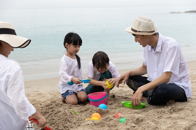 행복 한 아시아 가족 여름 휴가에 4 명 해변에서 모래에 장난감을 함께 연주 아침 시간에 일출입니다. 휴가 및 여행 개념.