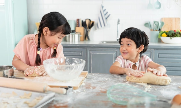 I bambini divertenti della famiglia asiatica felice stanno preparando l'impasto cuocere i biscotti in cucina