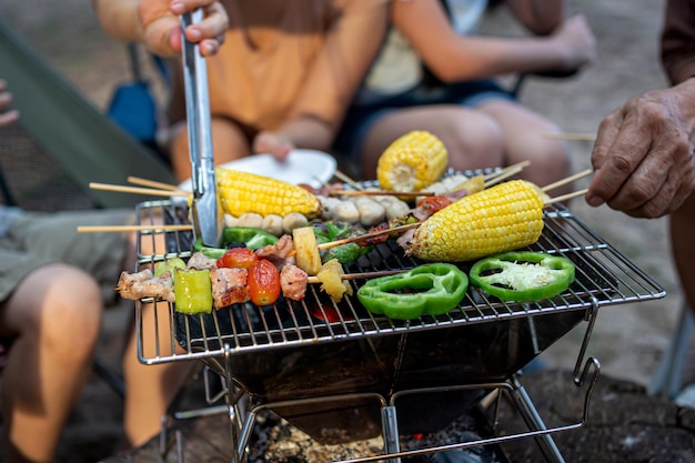 一緒にバーベキューをしている幸せなアジアの家族。夏のビーチでのキャンプ中に夕食のためにグリルバーベキューを調理します。