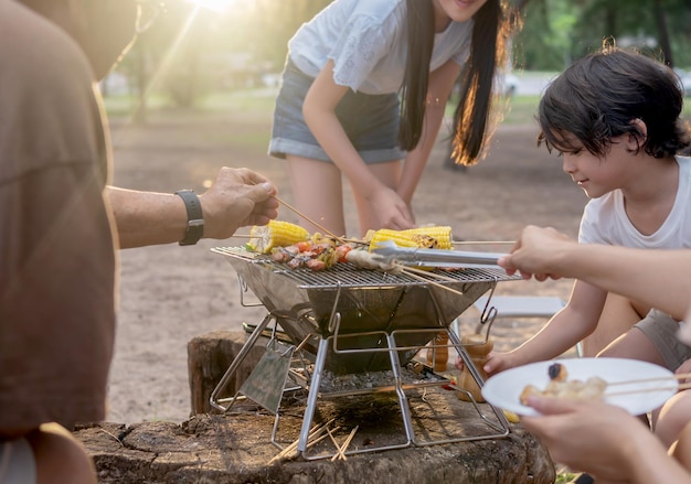 一緒にバーベキューをしている幸せなアジアの家族。夏のビーチでのキャンプ中に夕食のためにグリルバーベキューを調理します。