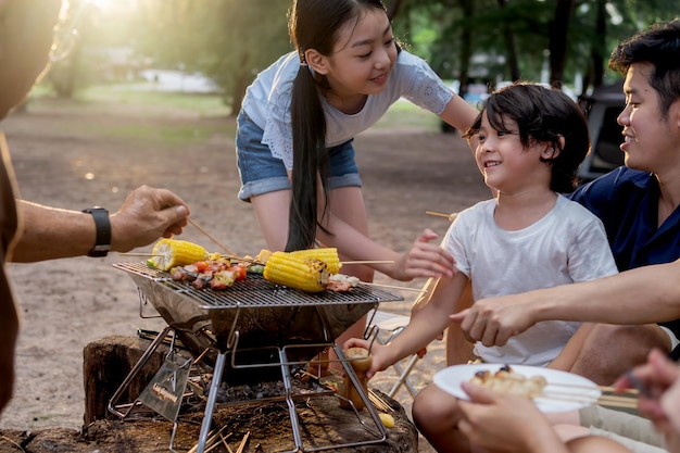 Happy asian family having barbecue together. cooking grilled\
bbq for dinner during camping on summer beach.